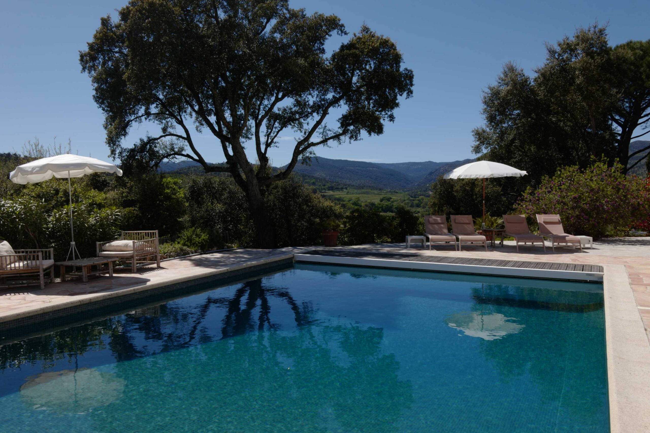 Vue sur la piscine avec transats, parasols et montagnes en arrière-plan